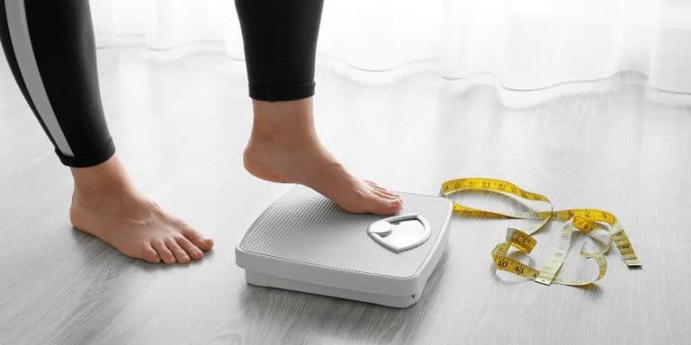 woman stepping on a scale with a measuring tape in front of the scale